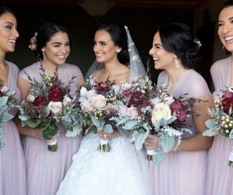 The bride with her bridesmaids smiling and holding flower bouquet