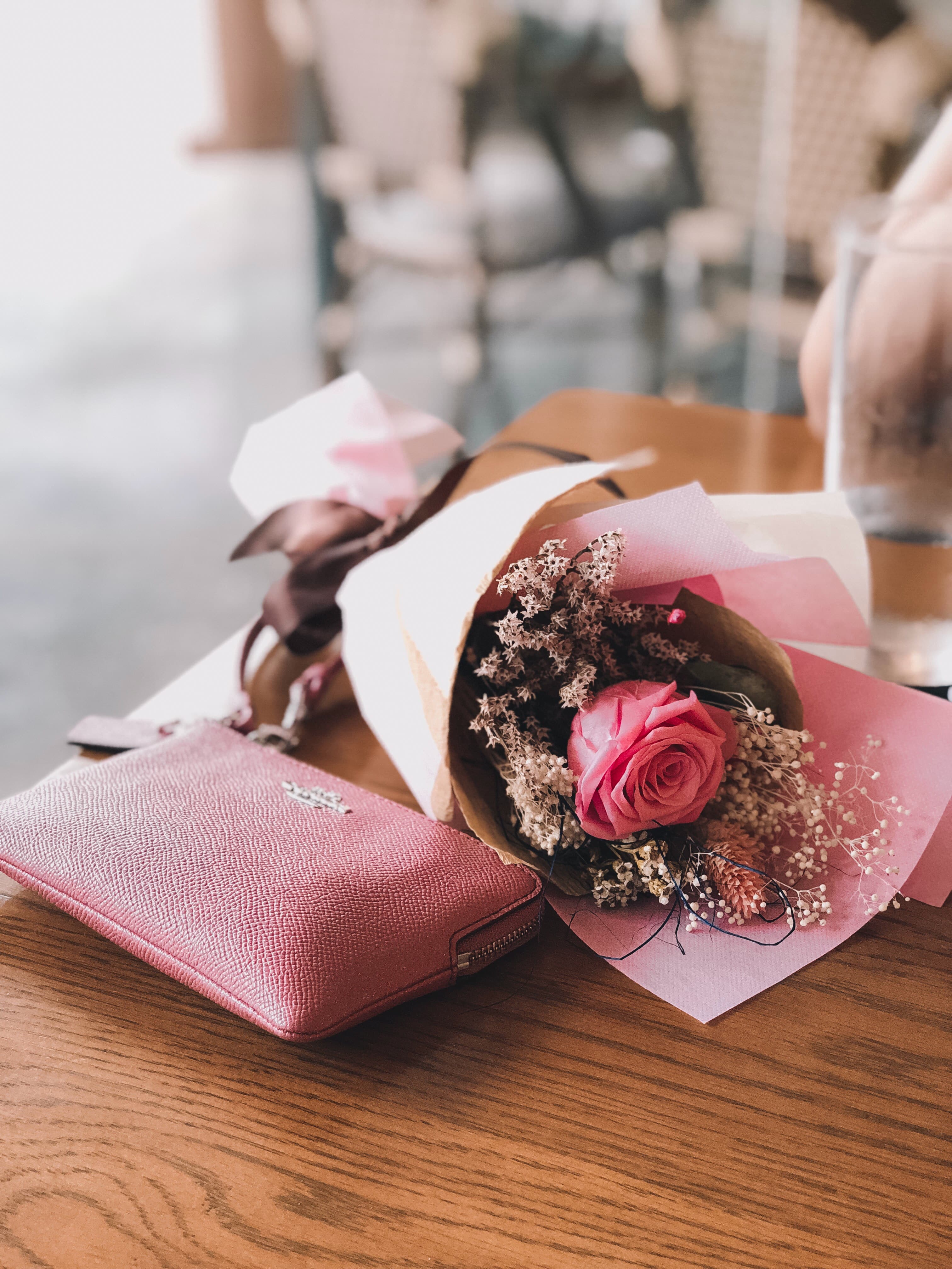 Pink Rose Flower near the Pink Coach Leather Wallet on a Wooden Table